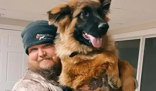 Jacob Robinson wearing a beanie holds a large, fluffy Leonberger or German Shepherd type dog with a black face and reddish-gold fur.